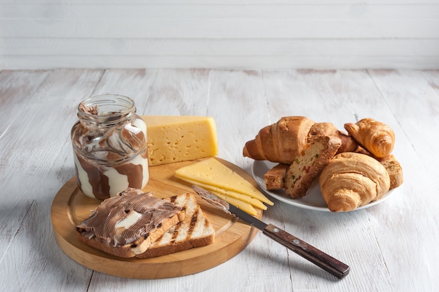 Frühstück Schokoladenbuttercreme und Croissant auf rustikalen Holzbrettern, Lebensmitteloberfläche.
