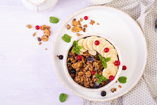 Frühstück. Schüssel selbst gemachtes Granola mit Joghurt und frischen Beeren. Sitzordnung bei Tisch. Gesundes Essen. Ansicht von oben.