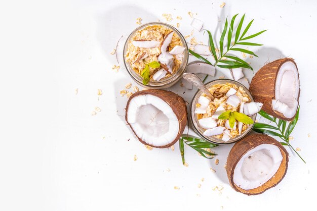 Frühstück über Nacht Haferflocken mit Kokosmilch und frischen Kokosnussstücken Diät gesunde Ernährung vegane Ernährung Auf hellem Hintergrund mit frischen Kokosnüssen und Palmblättern Kopierraum