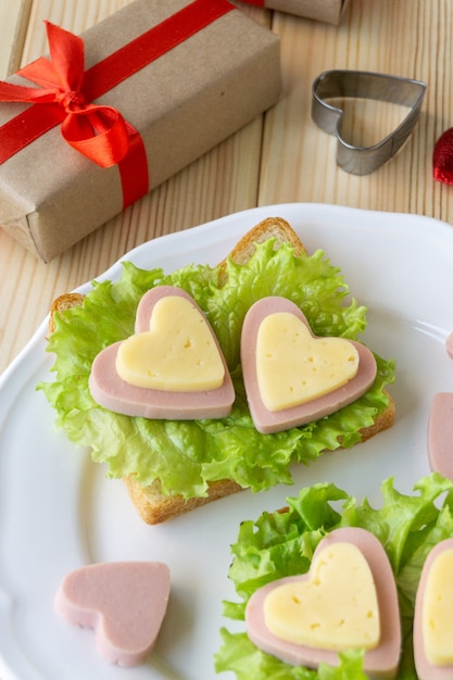 Frühstück zum Valentinstag. Sandwich mit Wurst, Käse und Salat auf weißem Teller.