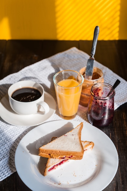 Frühstücken Sie mit Erdnussbutter und Stau und einem Tasse Kaffee auf einer Sonne des Holztischs morgens