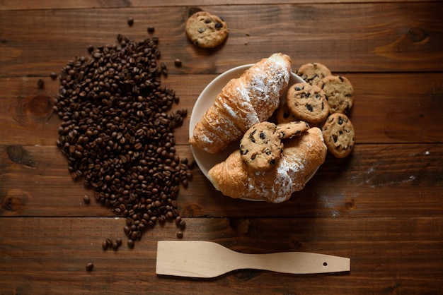 Frühstücks-Capuccino, Croissant und leckere Kekse auf einem Holztisch