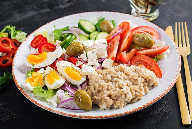 Frühstücks-Haferflockenbrei mit griechischem Salat aus Tomaten, Gurken, Oliven, Feta-Käse und Eiern. Gesundes ausgewogenes Essen.