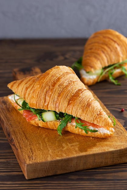 Frühstückscroissants-Sandwiches mit Lachs-Gurken-Frischkäse und Rucola auf einem Holzbrett