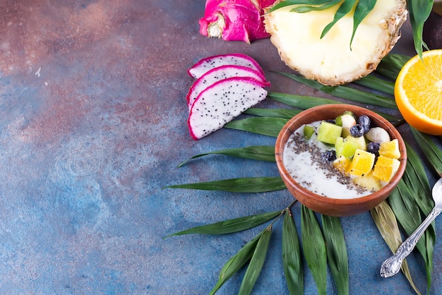 Frühstücksmoothieschüssel überstiegen mit pitaya, Ananas, chia Samen und Beeren mit Palmblatt auf Steinhintergrund, Draufsicht