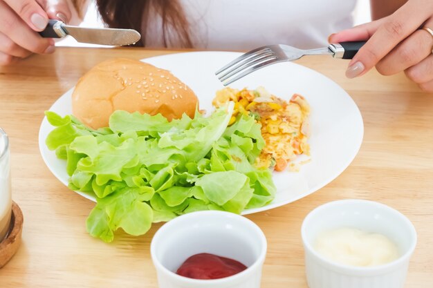 Frühstücksomelett, Brot, Hamburger und Gemüse auf einem weißen Teller mit Messer und Gabel essen