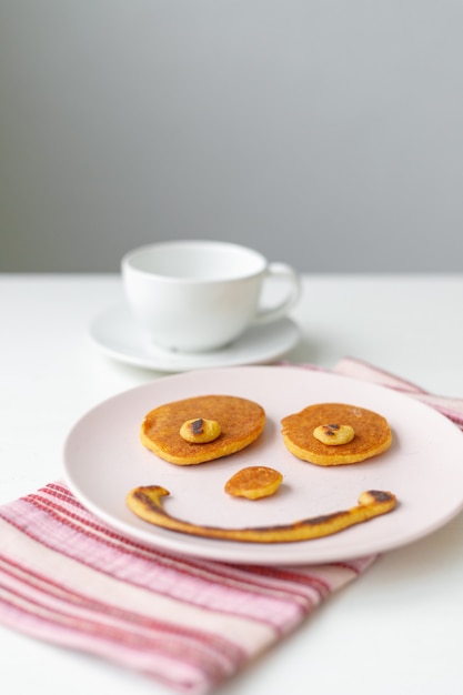 Frühstückspfannkuchen in Form eines Lächelns auf einem rosa Teller