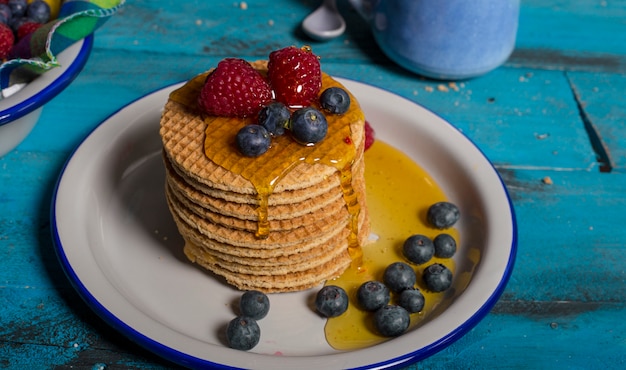 Frühstücksplatte der holländischen Waffeln mit Himbeeren, Blaubeeren und Honig auf hölzernem Hintergrund.