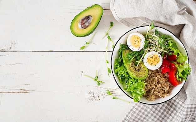 Frühstücksschüssel mit Haferflocken, Paprika, Avocado, Salat, Microgreens und gekochtem Ei.