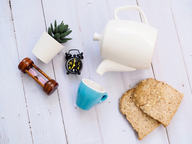 Frühstücksset mit Kaffeetasse aus Keramik, Teekanne, Wecker, Vollkornbrot und Kaktus-Zimmerpflanze.