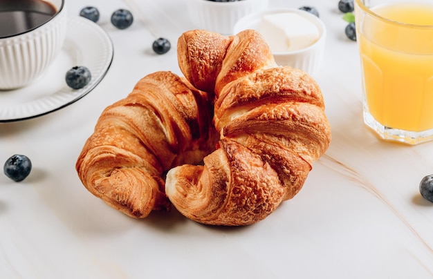 Frühstückstisch mit Croissants, Tasse Kaffee, Orangensaft und Beeren auf Marmorhintergrund. Selektiver Fokus