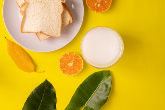 Frühstückstisch mit geschnittenem Brot und Glas Milch auf gelb