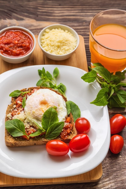 Frühstückstoast mit pochiertem Ei, Tomatensauce, Basilikum und Parmesan auf rustikalem Holz