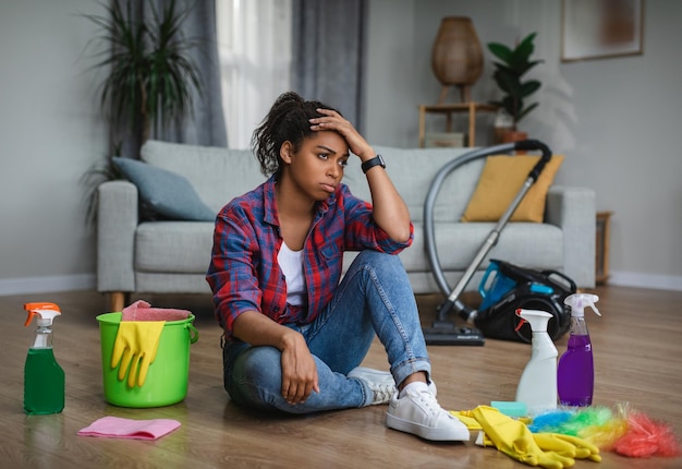 Foto frustrada e infeliz jovem dona de casa negra que sofre de muito trabalho doméstico sentada no chão