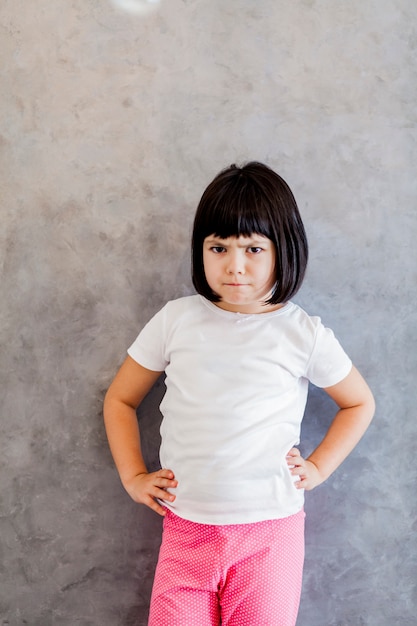 Frustrada niña de cabello negro junto a la pared