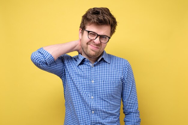 Frustrado jovem de camisa azul, segurando a mão no pescoço