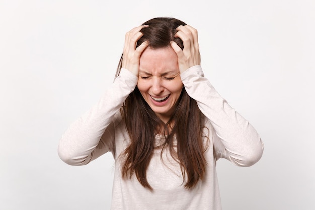 Frustrado llorando mujer joven insatisfecha con ropa ligera manteniendo los ojos cerrados, poniendo las manos en la cabeza aislada en el fondo de la pared blanca. Gente emociones sinceras concepto de estilo de vida. Simulacros de espacio de copia.