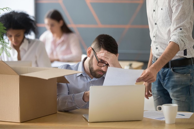 Frustrado, molesto empleado masculino que recibió un aviso de despido injusto al ser despedido del trabajo en el lugar de trabajo, deprimido, estresado, oficinista, a punto de empacar una caja el último día laboral, siendo despedido por concepto