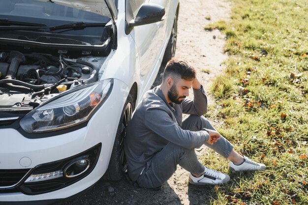 Frustrado, triste, molesto, el conductor del tipo está sentado cerca de un automóvil roto después de un accidente de tráfico.