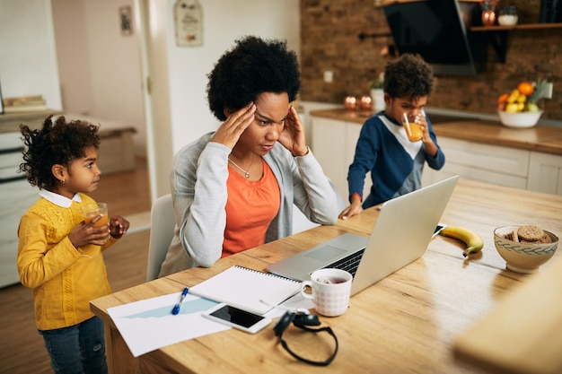 Frustrierte afroamerikanische alleinerziehende Mutter, die zu Hause am Laptop arbeitet