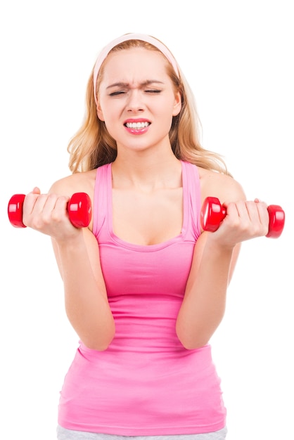 Frustrierte junge blonde Frau im rosa Hemd, die mit Hanteln trainiert