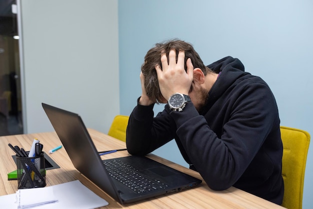 Frustrierter junger Mann, der im Büro an einem Laptop arbeitet Unternehmensberatung