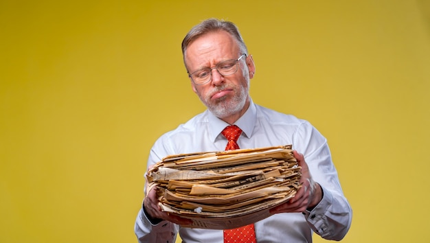 Frustrierter leitender Angestellter über gelbem Hintergrund überarbeitete Holdingstapel von Dokumentenpapierarbeit.