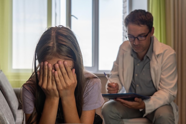 Frustriertes kleines Kind im Büro eines Psychologen Porträt eines Mädchens mit traurigem Gesicht, das während einer Therapiesitzung auf der Couch sitzt Therapeut versucht, einem unglücklichen, verbitterten Kind zu helfen, das Verhaltensprobleme hat