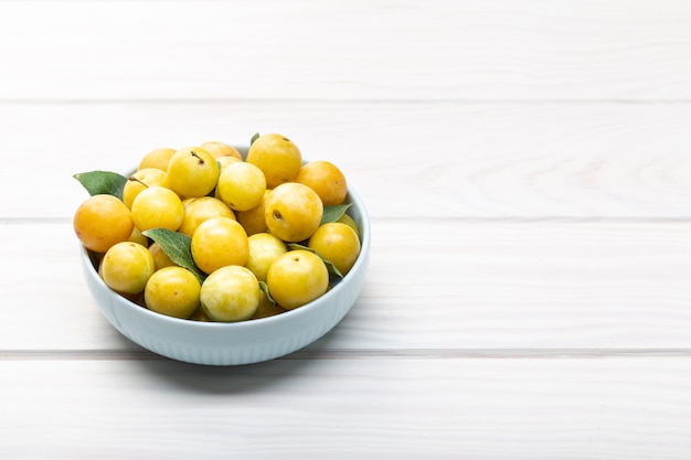 Fruta amarela mirabelle de ameixa em tigela na mesa de madeira branca. copyspace