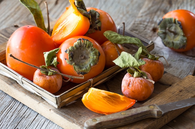 Foto fruta de caqui naranja madura. fruta caqui en mesa de madera. rodajas de caqui. conjunto de kakis. frutos del caqui kaki (diospyros kaki) en otoño japonés