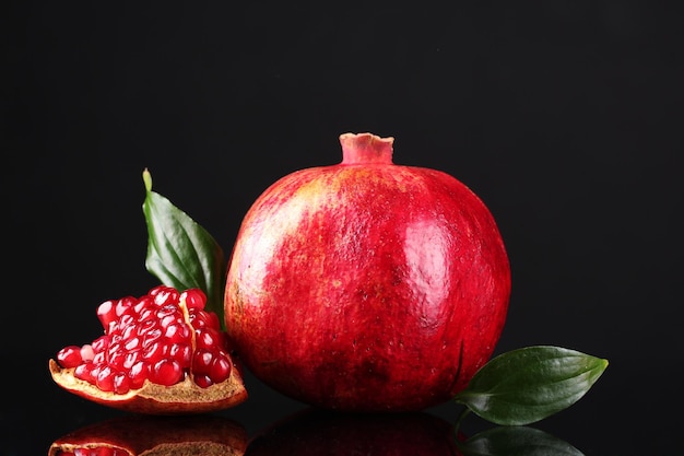 Fruta da romã madura com folhas em fundo preto