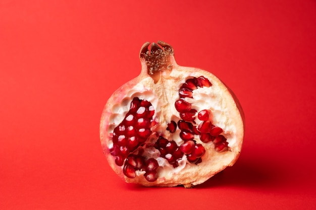Fruta da romã madura quebrada em uma superfície vermelha.
