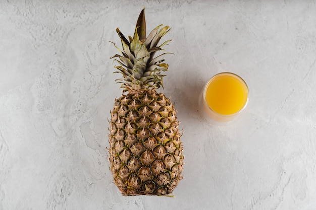 Fruta de abacaxi e suco em copo de vidro duplo na mesa de pedra branca. Frutas tropicais Derramando suco tropical amarelo no vidro.