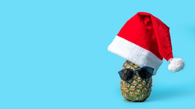 Fruta de abacaxi hipster na moda com óculos escuros e um chapéu de Papai Noel vermelho sobre um fundo azul
