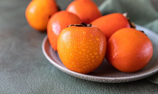 Fruta de caqui laranja madura com gotas de água sobre fundo verde de concreto