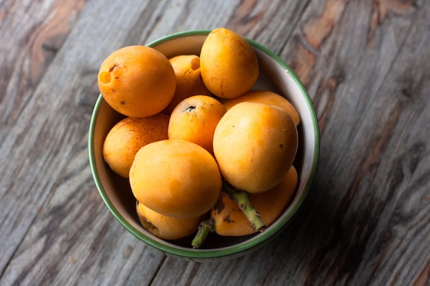 Fruta de nêspera madura eriobotrya japonica em copo verde na mesa de madeira vista superior