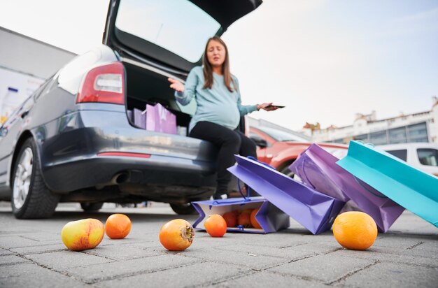 Foto fruta esparcida por el asfalto en el fondo de una mujer sentada en el maletero abierto de un coche