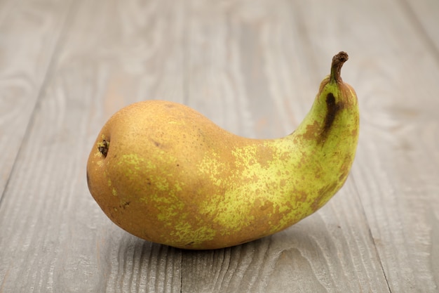 Foto fruta feia. uma forma de pêra feia em um fundo cinza com uma textura de madeira.