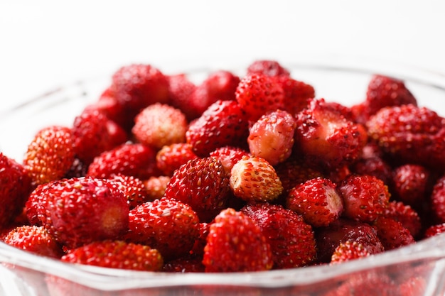 Fruta fresca de la fresa en un plato de cristal en un fondo blanco. De cerca.