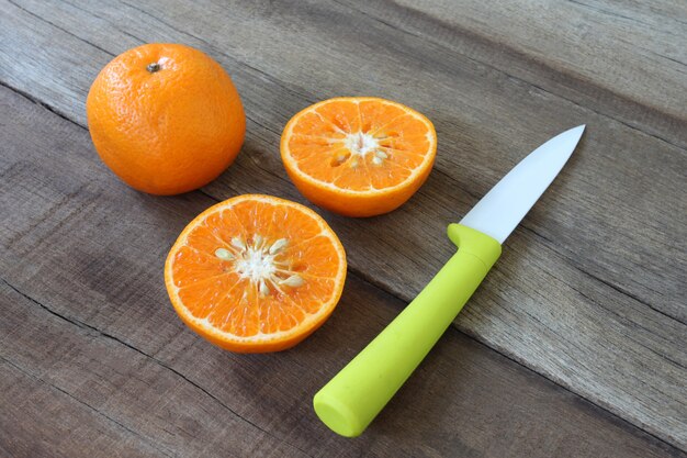 Fruta fresca de naranja colocada sobre suelo de madera y tiene cuchillo acrílico.