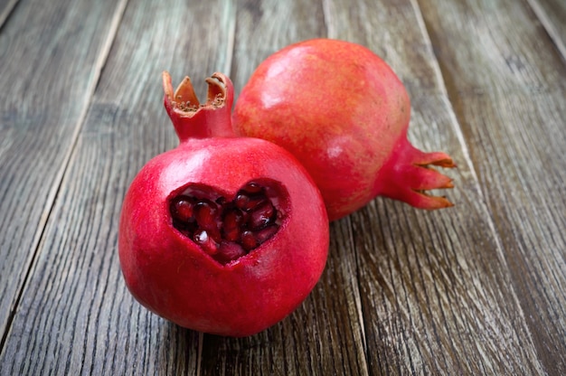 Fruta de la granada madura de cerca sobre fondo de madera. Concepto de alimentación saludable. Corte en forma de corazón sobre la piel de la granada.