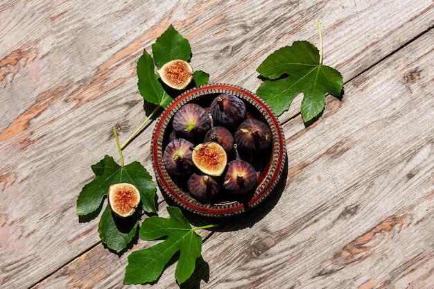 Fruta de higo púrpura madura con hojas en un recipiente de madera sobre fondo de madera