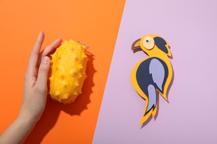 Foto fruta de kiwano en la mano y pájaro de papel en fondo naranja y púrpura vista superior