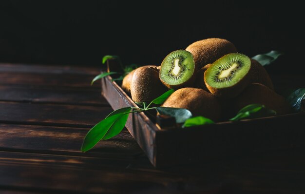 Fruta de kiwi fresca con hojas verdes en un cajón de madera en la mesa de madera.