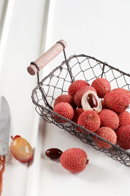 Fruta de lichi madura fresca y lichi pelado en una cesta de alambre sobre una mesa blanca de madera Espacio de copia