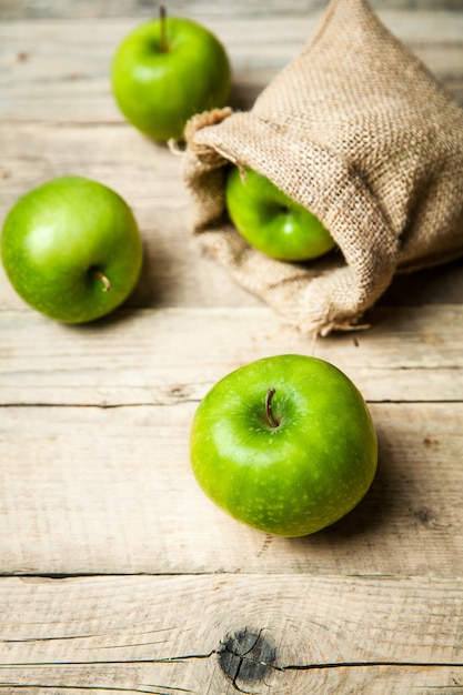 Fruta. Maçãs verdes maduras com serapilheira, na mesa de madeira