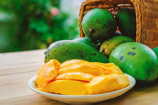 Fruta madura da manga na cesta na tabela de madeira com fundo verde borrado