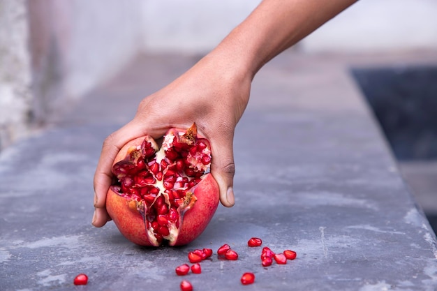 Foto fruta madura de romã na mão de uma mulher em fundo de concreto