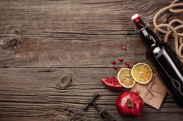 Fruta madura de granada con una copa de vino, una botella y un sacacorchos sobre un fondo de madera