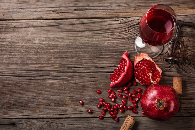 Fruta madura de granada con una copa de vino y un sacacorchos sobre un fondo de madera